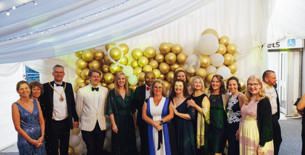 A group of staff, patients and representatives standing together in front of balloons at the Charity Ball event.