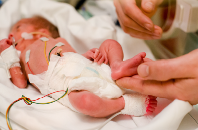 A newborn baby in the Neonatal Unit with a parent touching the baby's foot