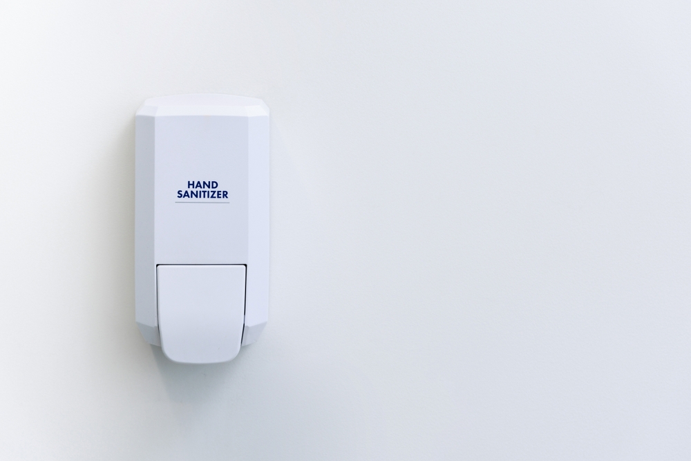 Wall-mounted hand sanitizer dispenser in a clinical hygiene station.