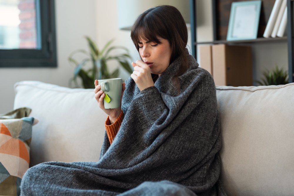 Shot of illness young woman drinking tea while sitting with a blanket on the couch at home