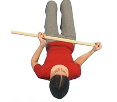 Person lying on back with broomstick in hands one hand is over end of stick elbows tucked in using stick to push operated arm out