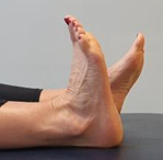 Feet with heels on bed toes pointing up, one foot flexed towards body