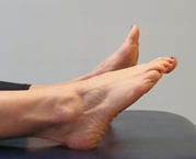 Feet with heels on bed toes pointing up, one foot pointed away from body