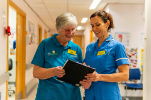 Photograph of a volunteer in a hospital setting talking and smiling to a nurse. 