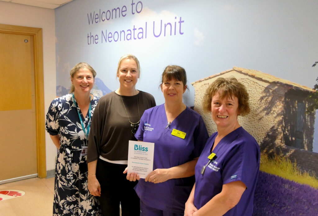 Members of the neonatal team stand together outside the Neonatal Unit, with one holding a Bliss Baby Charter Gold accreditation certificate.