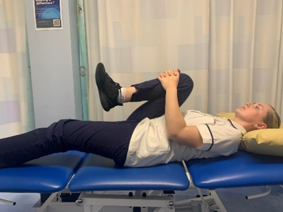 A picture of a person lying on their back on a bed, bringing one leg up and hug it towards the chest.