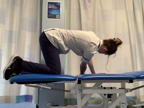 A person on hands and knees on the bed. Thread one hand through underneath to the opposite side.