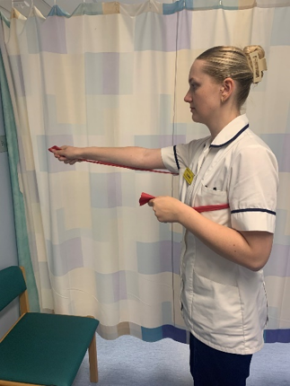 A picture of a person standing, holding each end of the band in your hands. Slowly, one arm at a time, extend your elbow to straighten the arm up towards shoulder height, pushing against the band.
