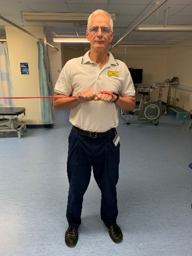 A picture of a person, standing holding the exercise band which is attached firmly to something secure.