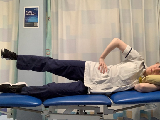 A picture of a person lying on their side. Placed the upper hand on the hip. Keeping your knee straight, slowly raise the upper leg away from the other