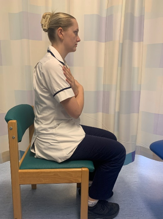 A picture of a person sitting on a chair with the arms over the chest.