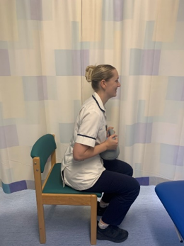 A picture of a person sitting on a chair, holding a weight.